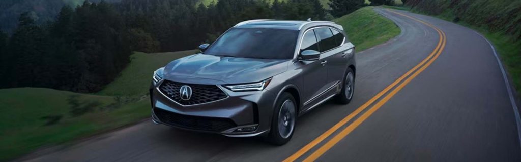 2025 Acura MDX driving on a scenic winding road, showcasing its sleek exterior design, luxury styling, and confident performance.