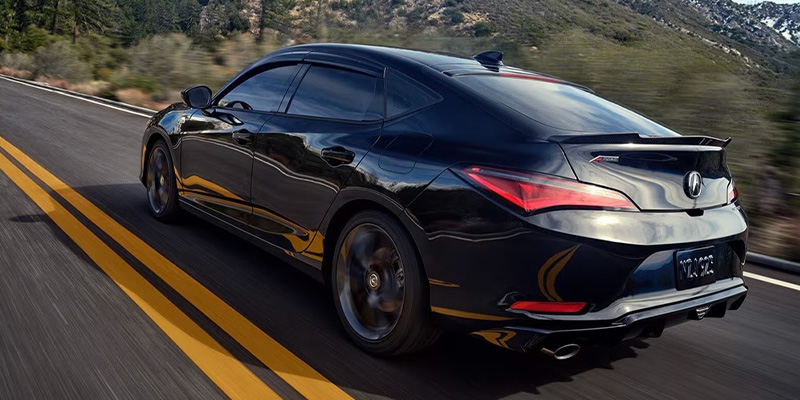 A sleek black sports sedan driving on a winding road with mountains in the background.