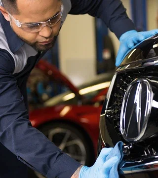 Acura-trained technician in safety glasses and gloves working on the front of an Acura in the shop